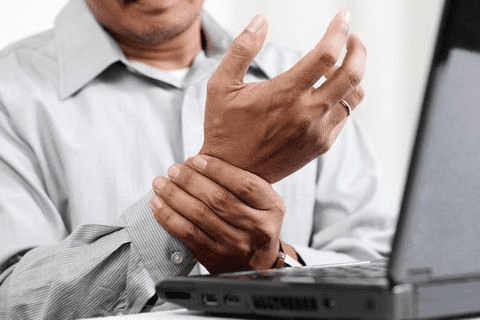 a man sitting at his laptop holding his wrist in pain