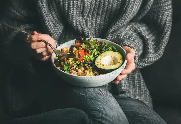Woman in sweater eating fresh salad, avocado, beans and vegetables Woman in sweater eating fresh salad, avocado, beans and vegetables