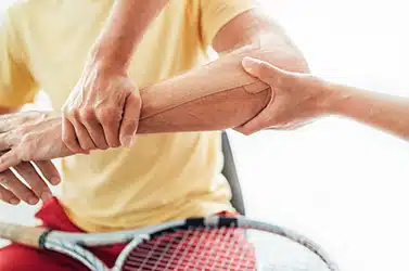 Tennis player elbow taped with elastic therapeutic or Kinesio tape applied by nurse at orthopedic ward close up image. Active sporty people health rehabilitation concept image. Tennis player elbow taped with elastic therapeutic or Kinesio tape applied by nurse at orthopedic ward close up image. Active sporty people health rehabilitation concept image.